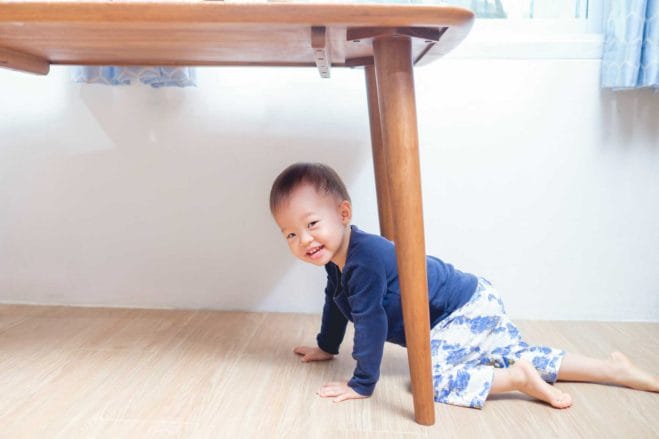 cute smiling Asian toddler boy playing at a table at home, looking at the camera with a playful expression, representing happy childhood.