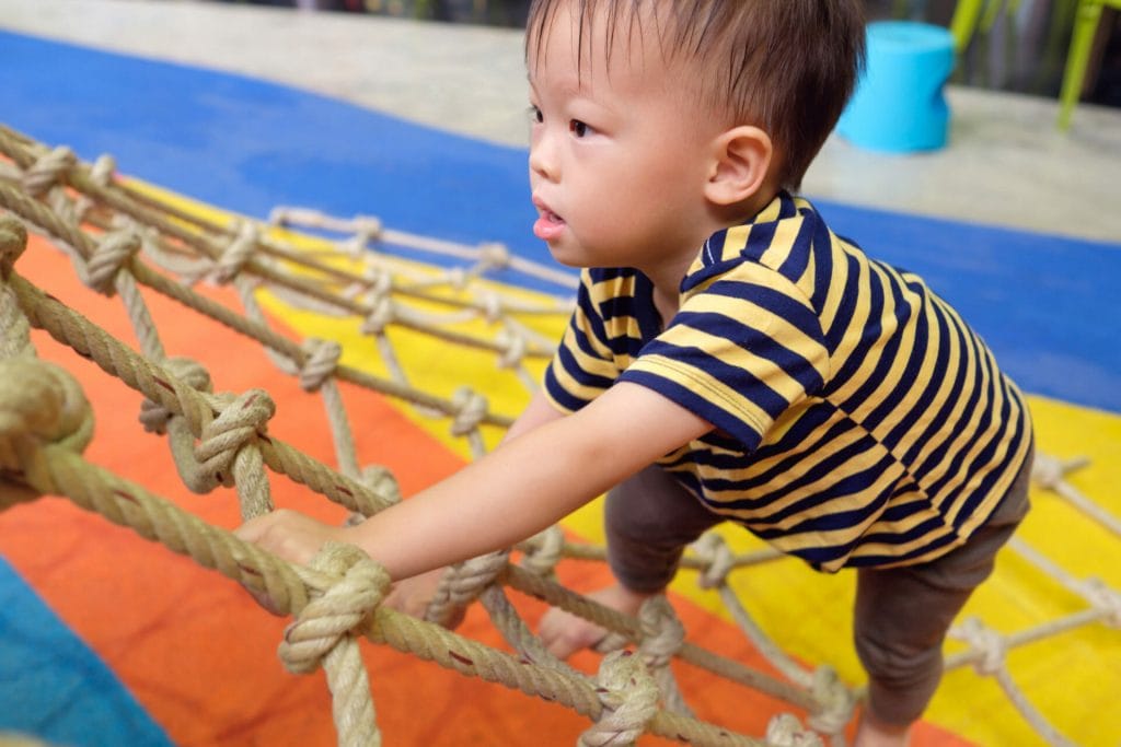 Cute little asian 2 years old toddler baby boy child having fun trying to climb on jungle gym at indoor playground