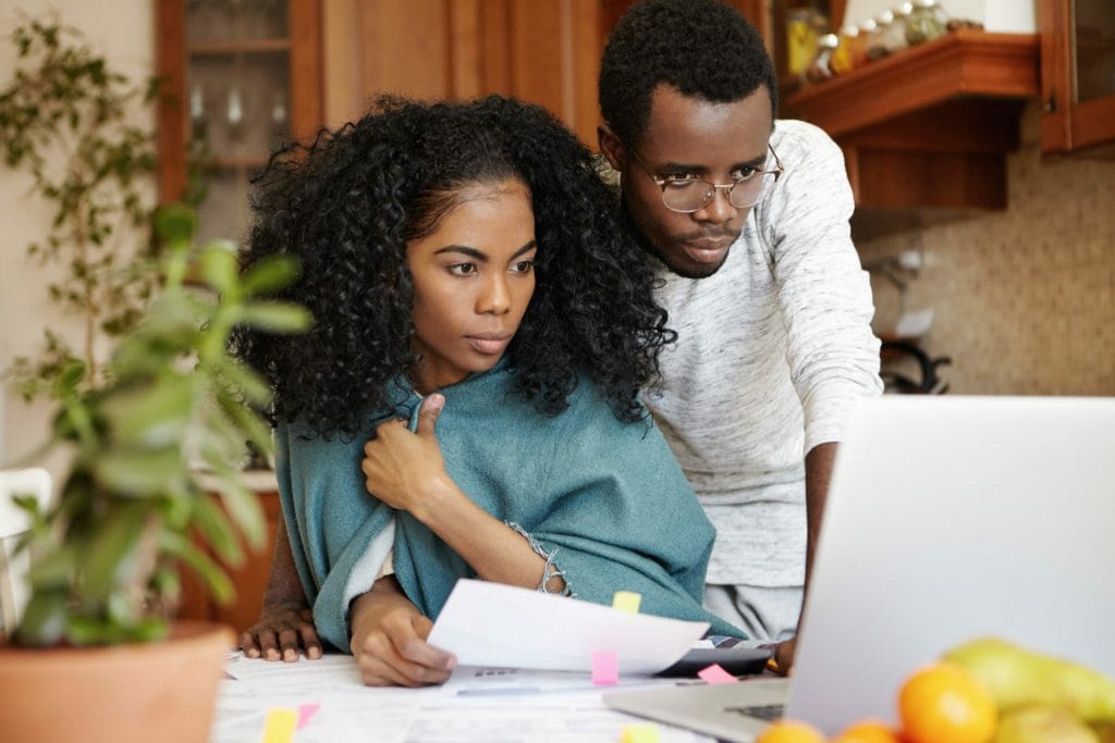 Financial problems, family budget and debts. Frustrated young African husband and wife using laptop pc while doing paperwork together, calculating expenses, managing bills in their modern kitchen