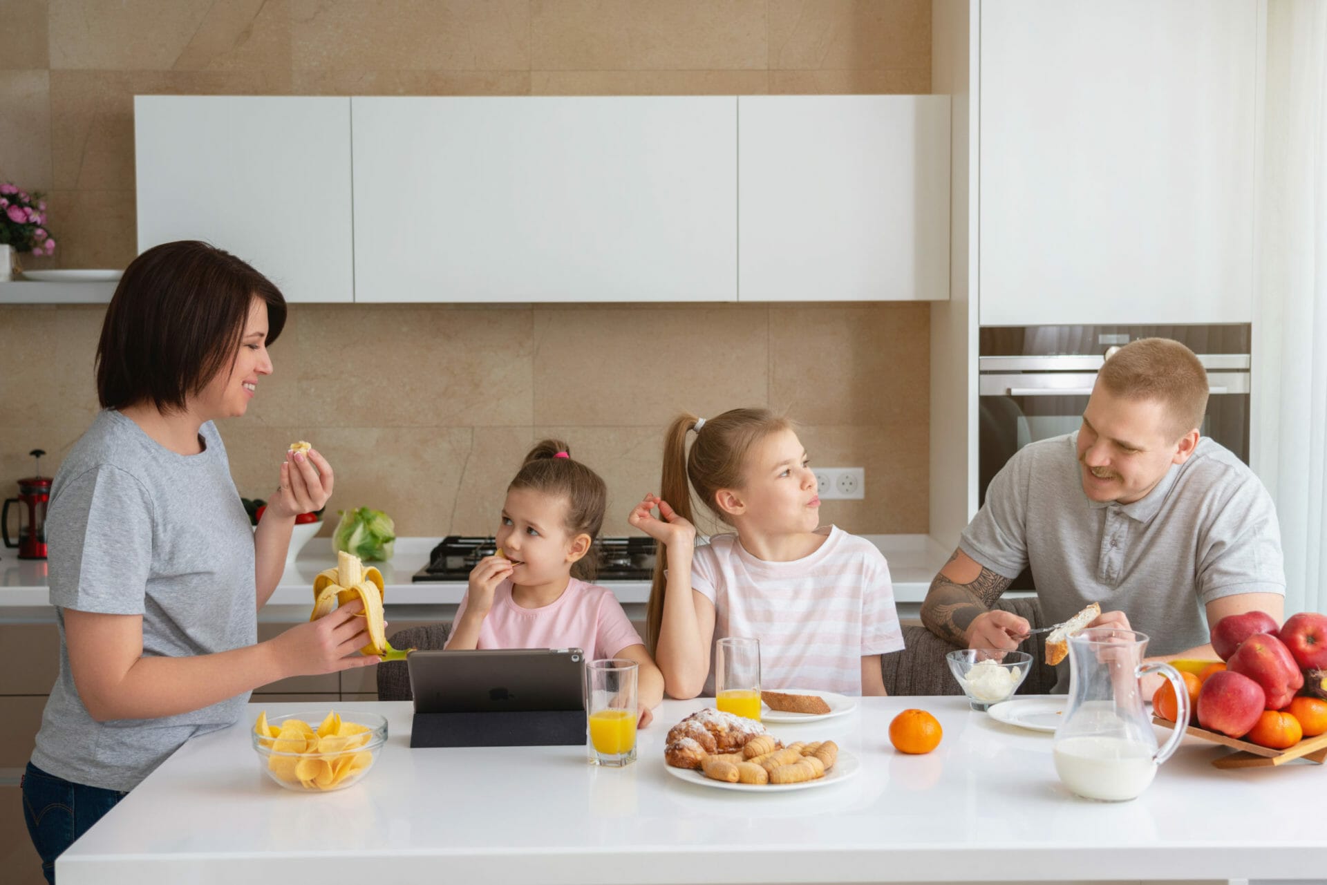 Smiling family dining together at kitchen table and having fun, parents with two daughters