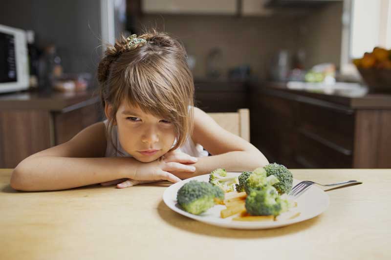 Upset girl looking at broccoli with disgust