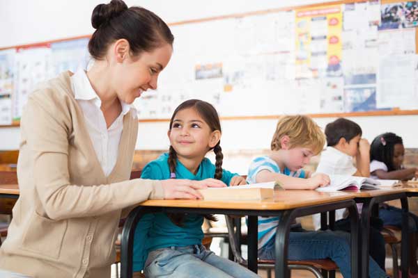 Pretty teacher helping pupil in classroom