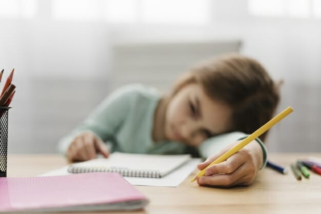 bored little girl resting her head while doing her homework