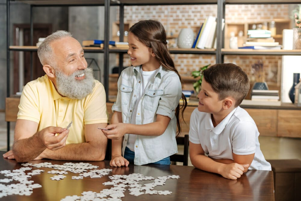 best cooperation smiling happy senior man his beloved grandchildren doing jigsaw puzzle uniting three pieces puzzle together
