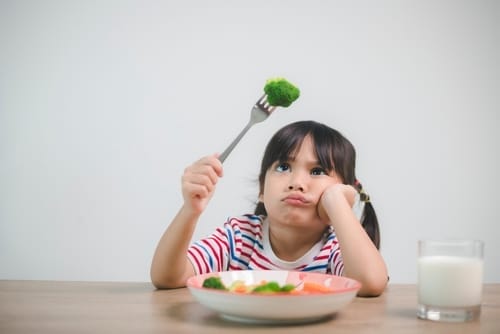 Unhappy girl eating healthy but tasteless food, broccoli lying on table, diet